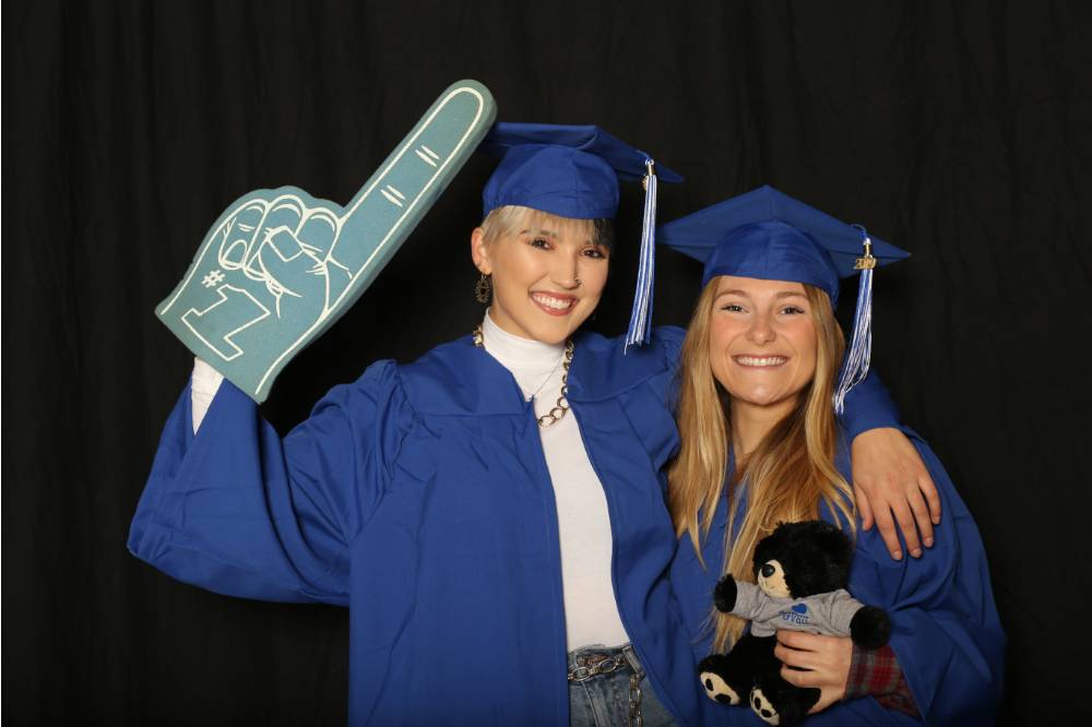 two students posing with foam finger and stuffed bear